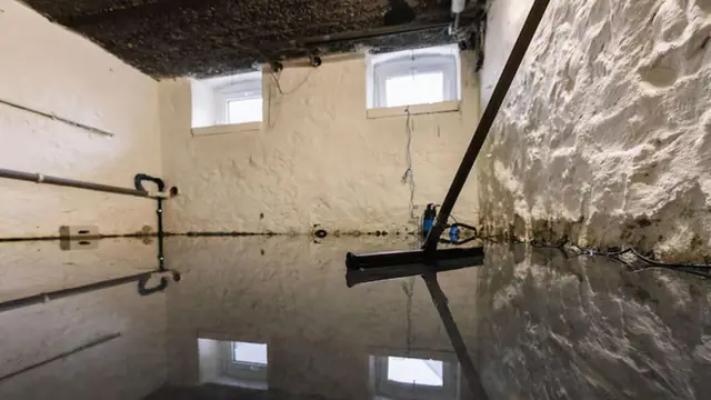 Basement with standing water and a squeegee against a damp wall
