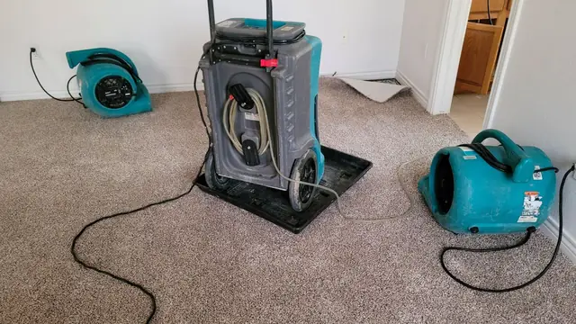Dehumidifier and air movers drying a carpeted room after water damage